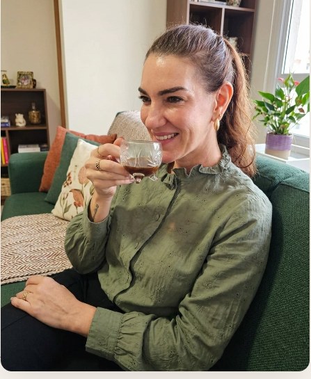 Lúcia Zamboni sentada no sofá, tomando um café